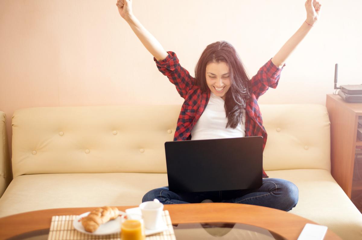 Woman smiling with arms in the air at laptop