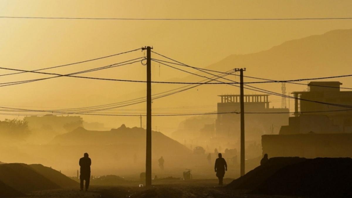 yellow lit photo of electric poles and wires in a dusty area of kabul, afghanistan with mountains barely visible in the background and silouhettes of two people