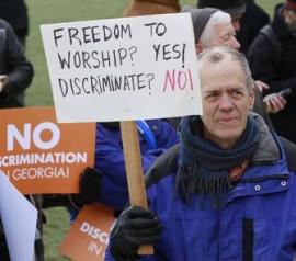 Man holding protest sign saying 'FREEDOM TO WORSHIP? YES! DISCRIMITE? NO!'