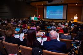 Photo from back of the room at Ethics Conference, showing audience from behind and frontal view of presenters at podium