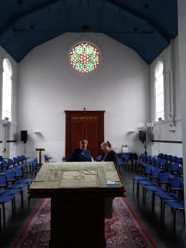 Vaulted synagogue interior with stained glass, two rabbis seated in the center