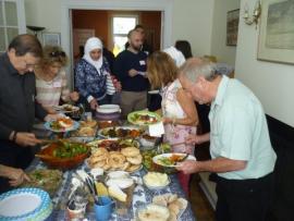 Syrian famillies and hosts gather around potluck table laden with food