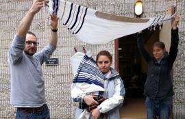 Women carrying Torah out of synagogue building, walking under tallit held by a woman and a man