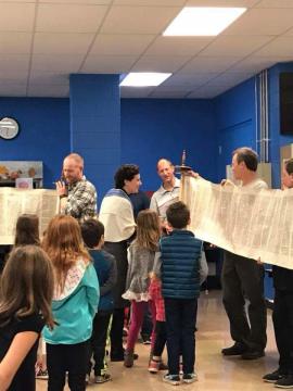 Families examining unfurled Torah scroll