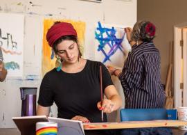 Art student with Rabbi Rebecca Richman painting in center, student artwork hanging in background