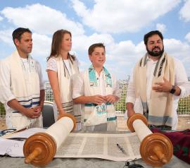 Bar mitzvah and family in front of Torah scroll with Israeli cityscape in background