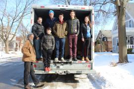 Adults and teens stand in the open back of a cargo truck amid winter snow