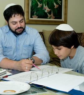 Man seated at table with teenage bar mitzvah student, pointing out words on a text in a binder