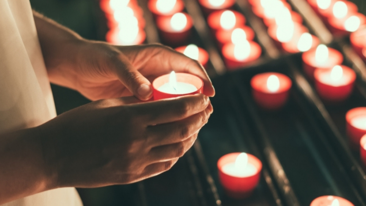 A person holding a lit candle near rows of other lit candles at a memorial