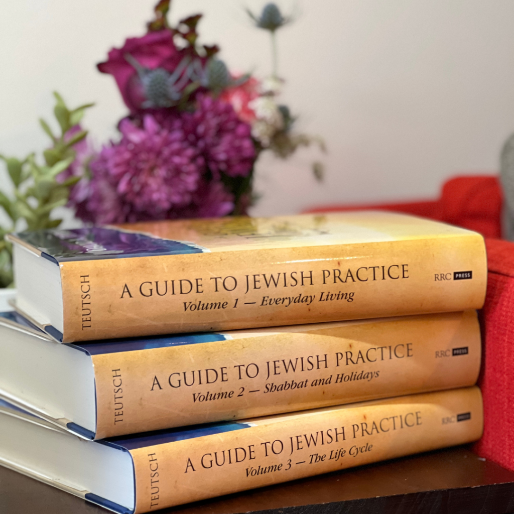 Stack of three books titled A Guide to Jewish Practice with flowers in the background.