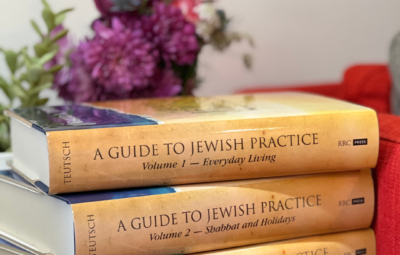 Stack of three books titled A Guide to Jewish Practice with flowers in the background.