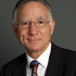 A man in a suit and colorful tie smiles against a gray background.