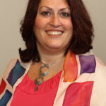 Smiling woman with shoulder-length hair, wearing a colorful shawl over a pink top.