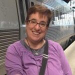 Person in a purple shirt smiling near a train.