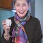 Smiling woman holding a silver cup, wearing a colorful scarf and dark top.