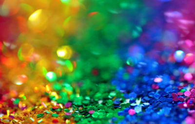 Colorful, sparkling glitter in a gradient pattern of rainbow hues, creating a vibrant and festive background.