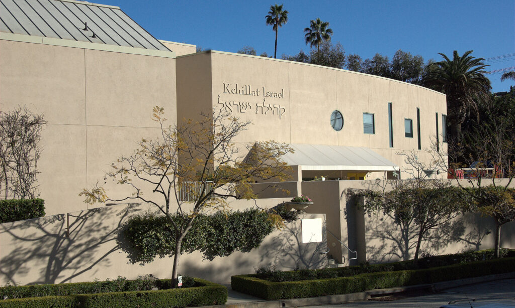 Exterior of a beige building with Kehilat Israel written on it, surrounded by trees and bushes.