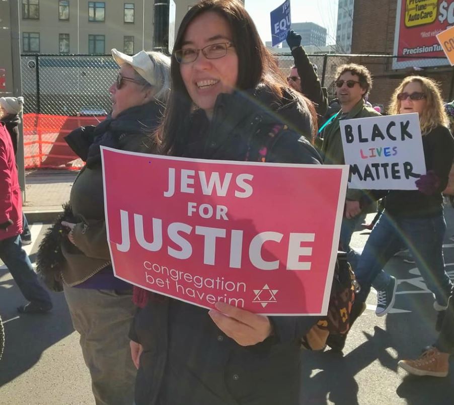 Person holding a Jews for Justice sign at a protest, with others holding Black Lives Matter signs in the background.