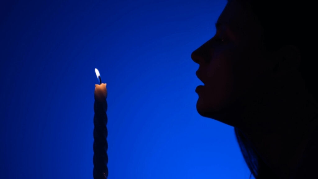 Silhouette of person's head with single lit candle