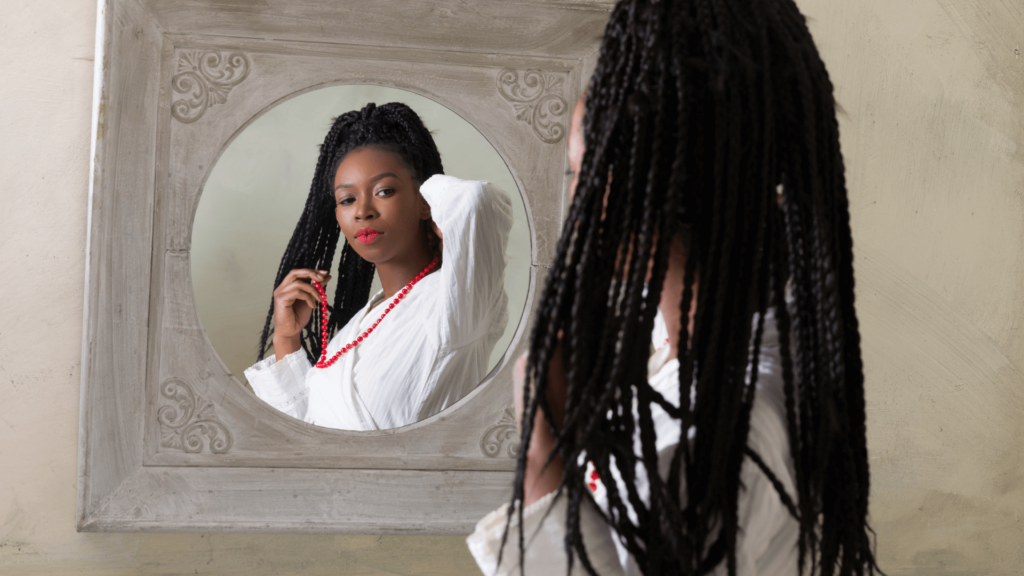 Black woman putting on a red necklace looking in the mirror