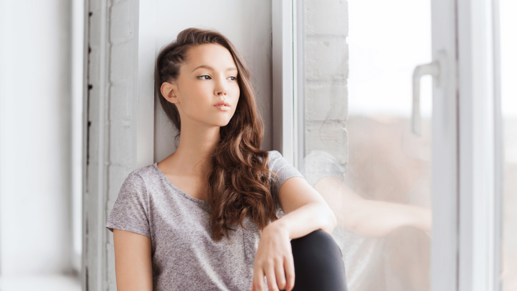 A woman with long brown hair looking out a large window