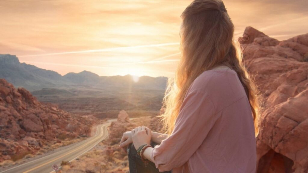 Woman sitting roadside in the desert looking off into the sunset