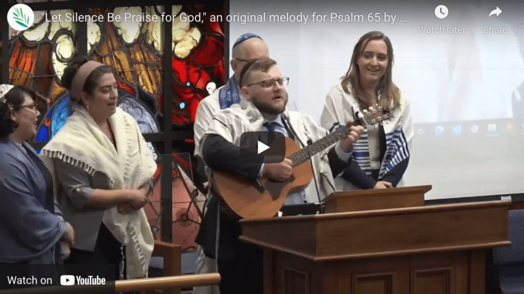 Screenshot of rabbi singing and playing guitar on the bimah