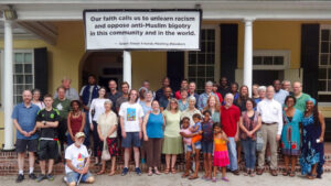 A diverse group poses in front of a building with a sign promoting racial and religious inclusion.