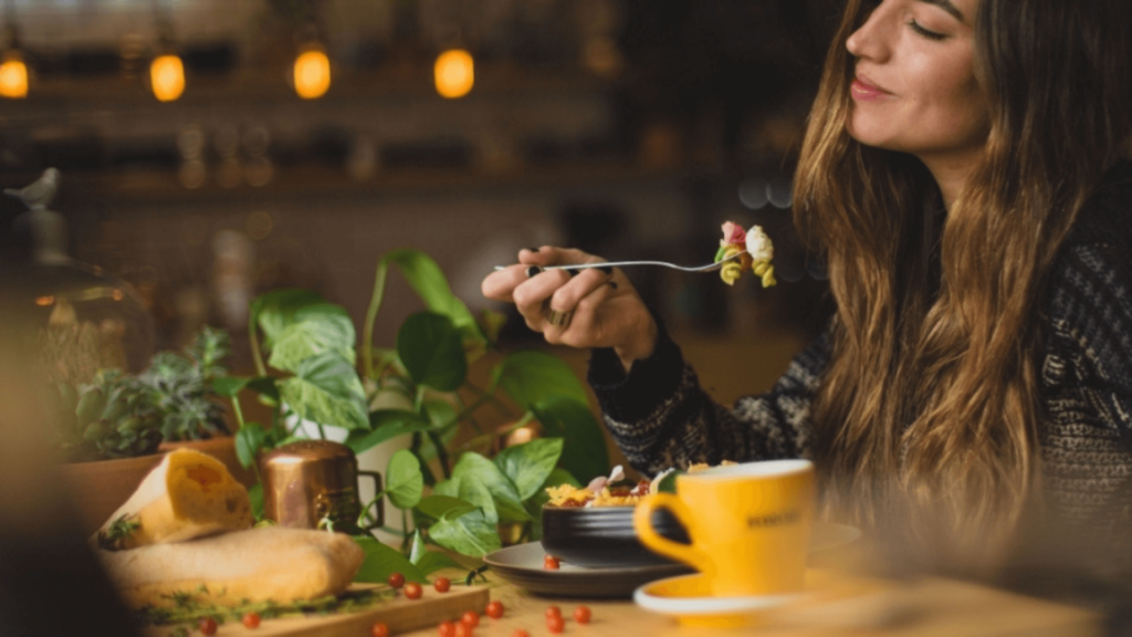 White woman with long hair smiling and eating pasta