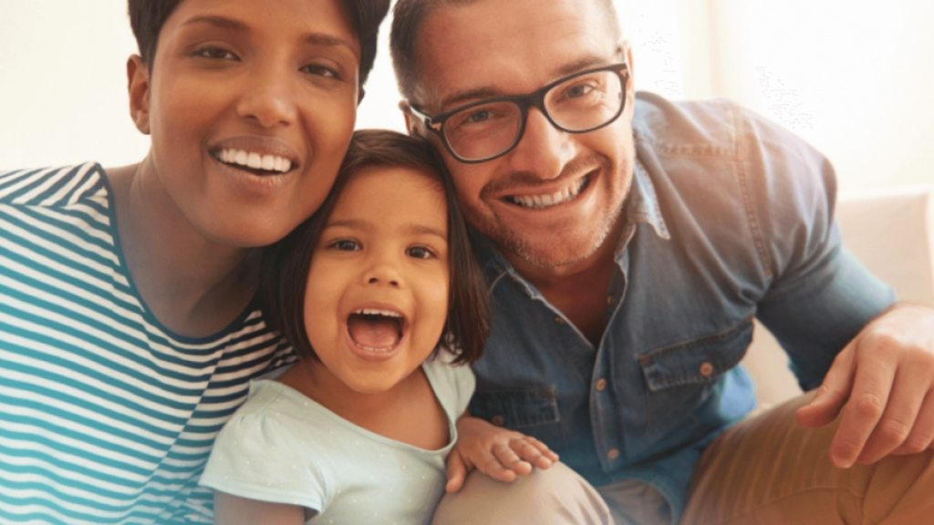 A multi-ethnic family with two parents and a little girl smiling