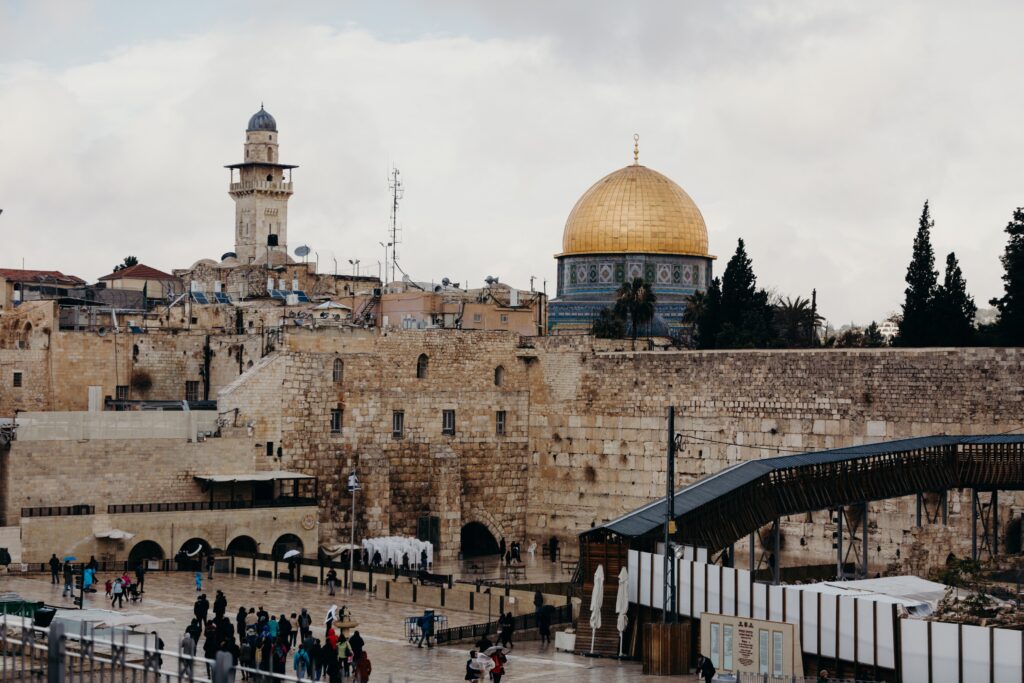 View of the Western Wall and Dome of the Rock in Jerusalem, with people walking nearby.