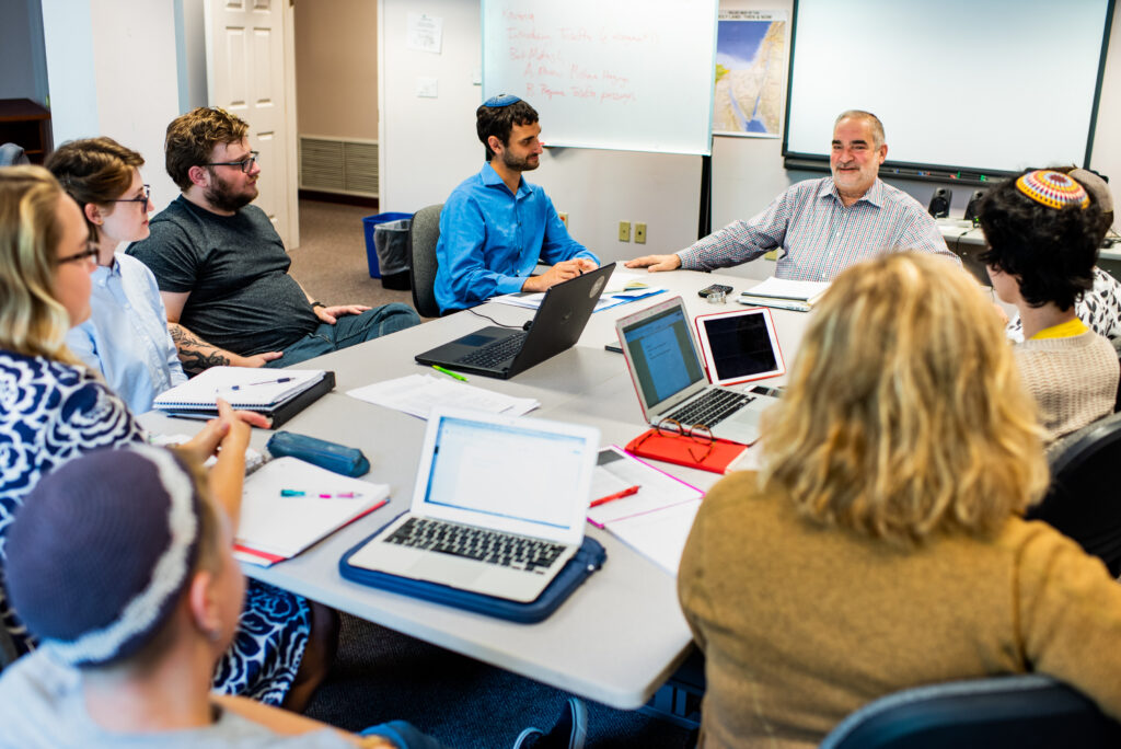 Rabbi Jacob Staub and students learn at a table in an RRC classroom in a photo taken before the pandemic. 