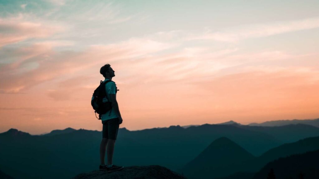 Silhouetted person with backpack pausing mid-hike in front of sunset