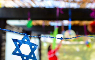 Blue Star of David hanging, with a blurred person in red in the background and colorful decorations around.