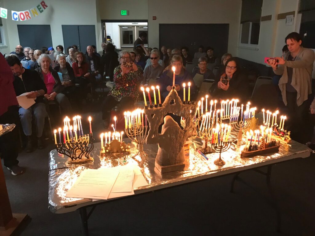 Congregants gather around a table of lit menorahs.