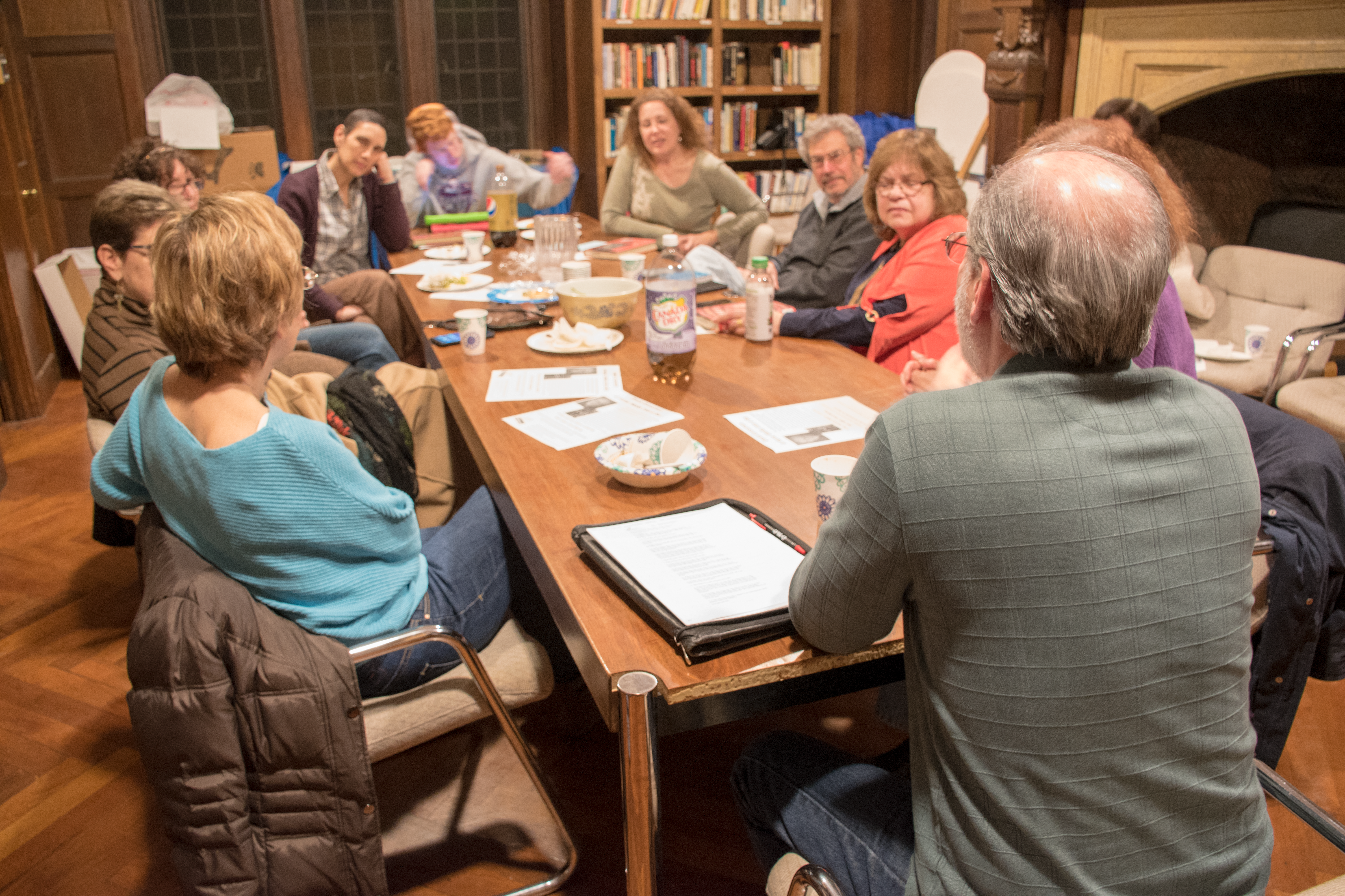 A group of members sit around a long, wooden table. Books are open, covering much of the surface.