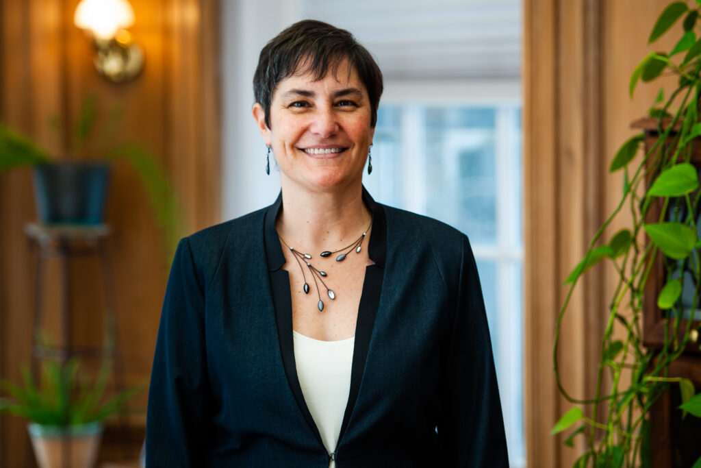 A waist up photo of Rabbi Deborah Waxman smiling in her office.