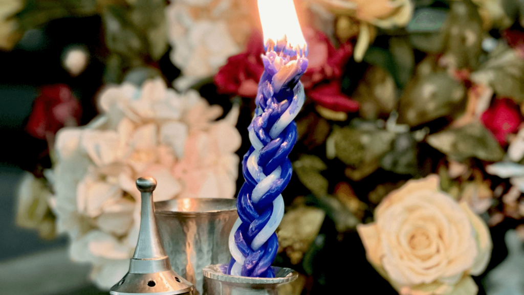 A lit havdalah candle in front of a bouquet of flowers