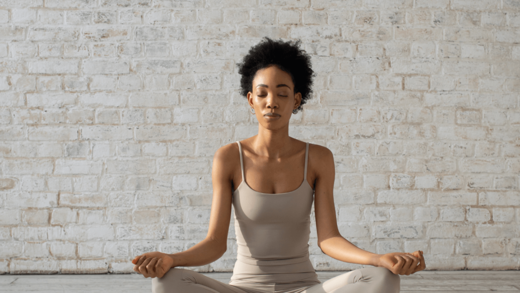 A Black woman meditating in front of a white brick wall