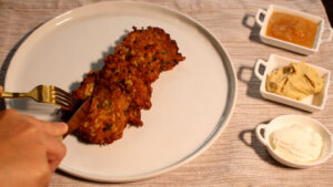 Person cutting open aruk (Iraqi latke) next to apple sauce, hummus and sour cream.