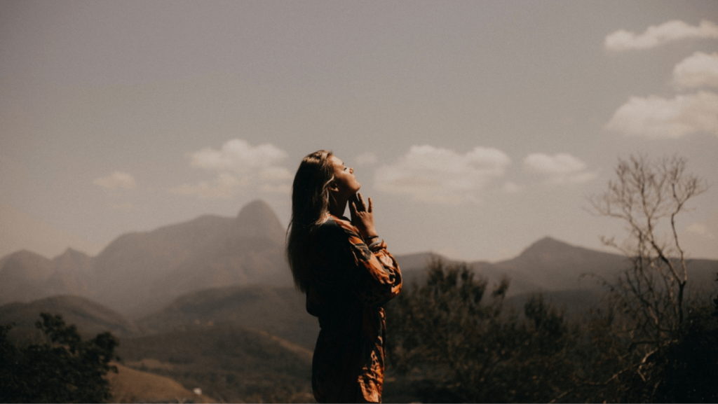 Young woman with her eyes closed standing outside with mountains in the background