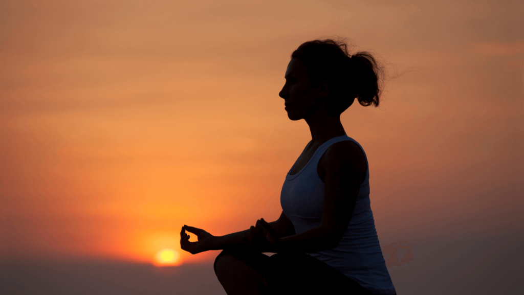 Silhouette of young woman meditating outside at sunrise