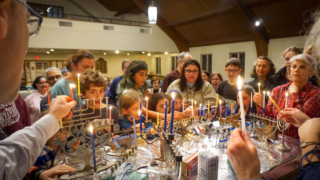 Families at Temple Beth Israel of Media stand and simultaneously light a many menorahs