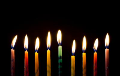 Nine colorful lit candles lined up against a dark background.