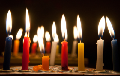 Lit candles of various colors burning in the dark.