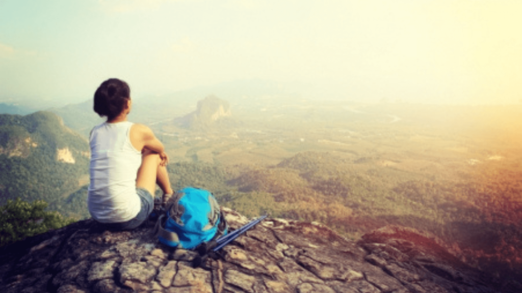 Person sitting on a mountaintop looking out over a mountain range