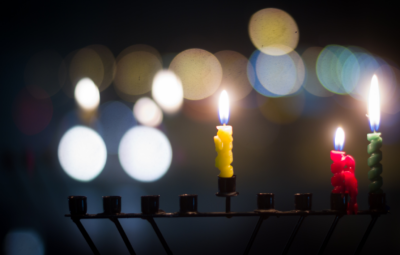 Three colorful candles lit on a menorah with blurred lights in the background.