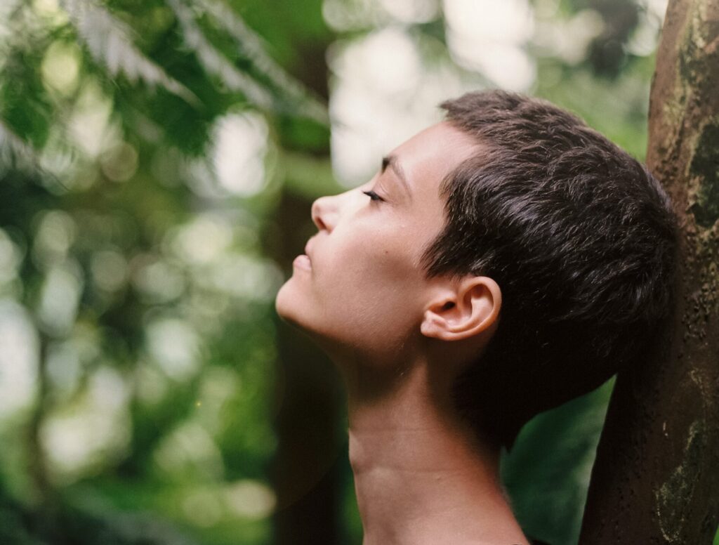 woman with short hair with her eyes closed in a wooded area