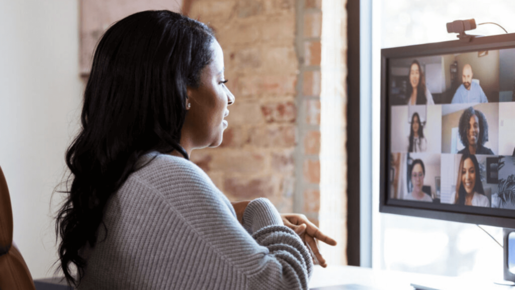 A Black woman on a video call with six other people on a desktop computer