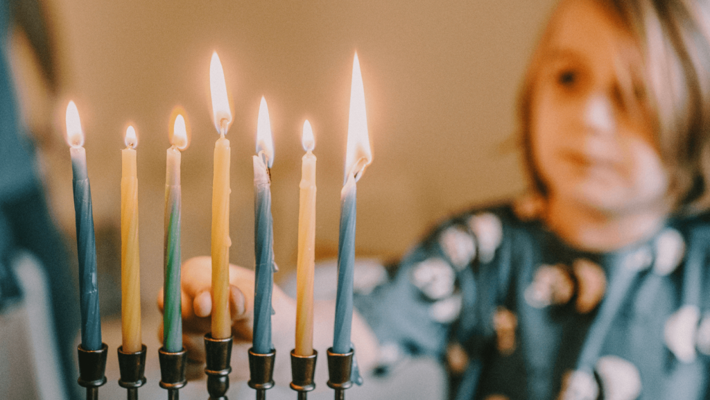 A young child lighting a menorah with 7 candles